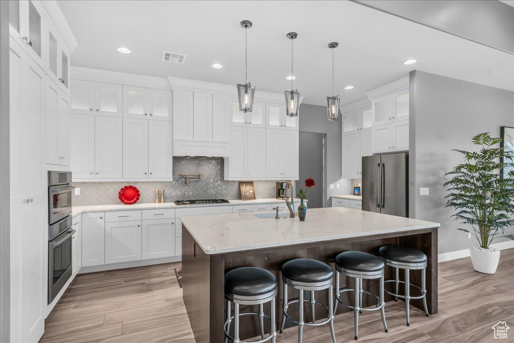 Kitchen with appliances with stainless steel finishes, a sink, light wood-type flooring, a center island with sink, and recessed lighting