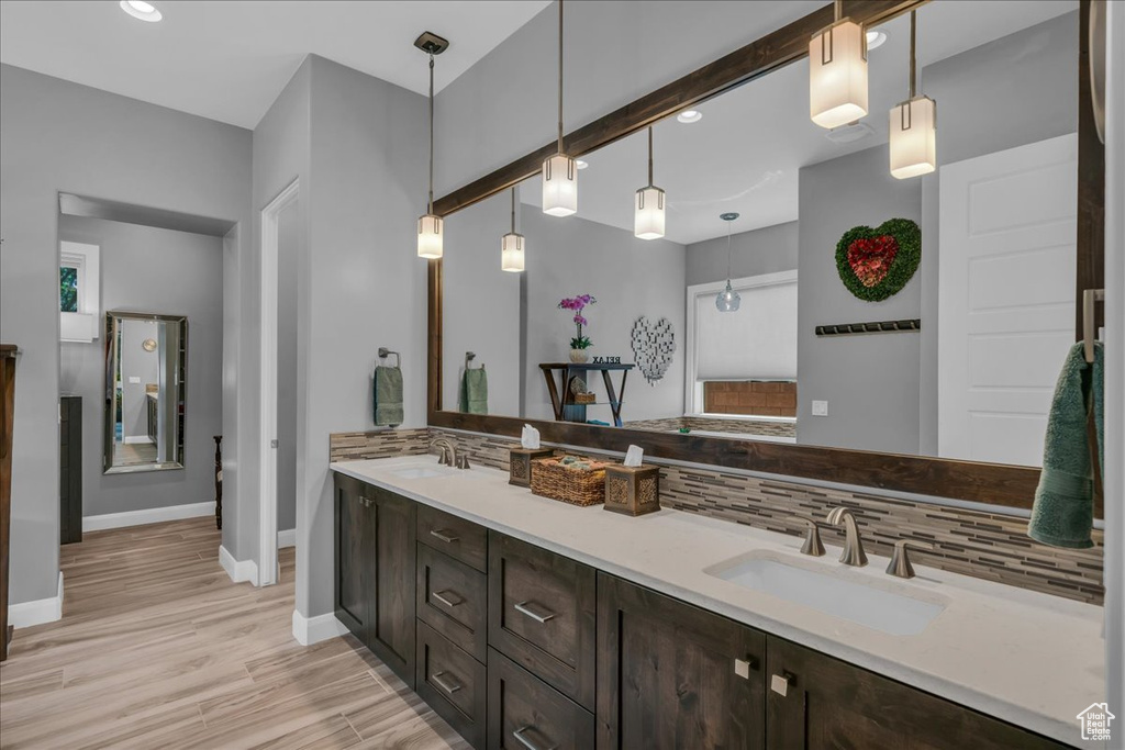 Full bath with baseboards, tasteful backsplash, double vanity, wood finished floors, and recessed lighting