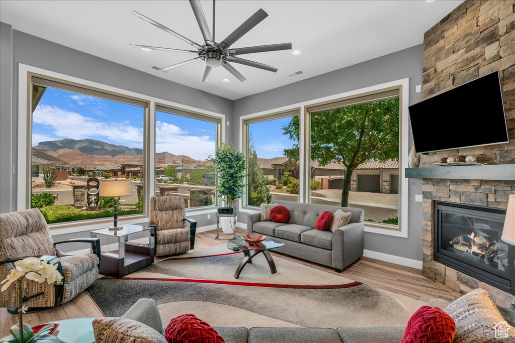 Living area featuring a stone fireplace, wood finished floors, a ceiling fan, baseboards, and a mountain view