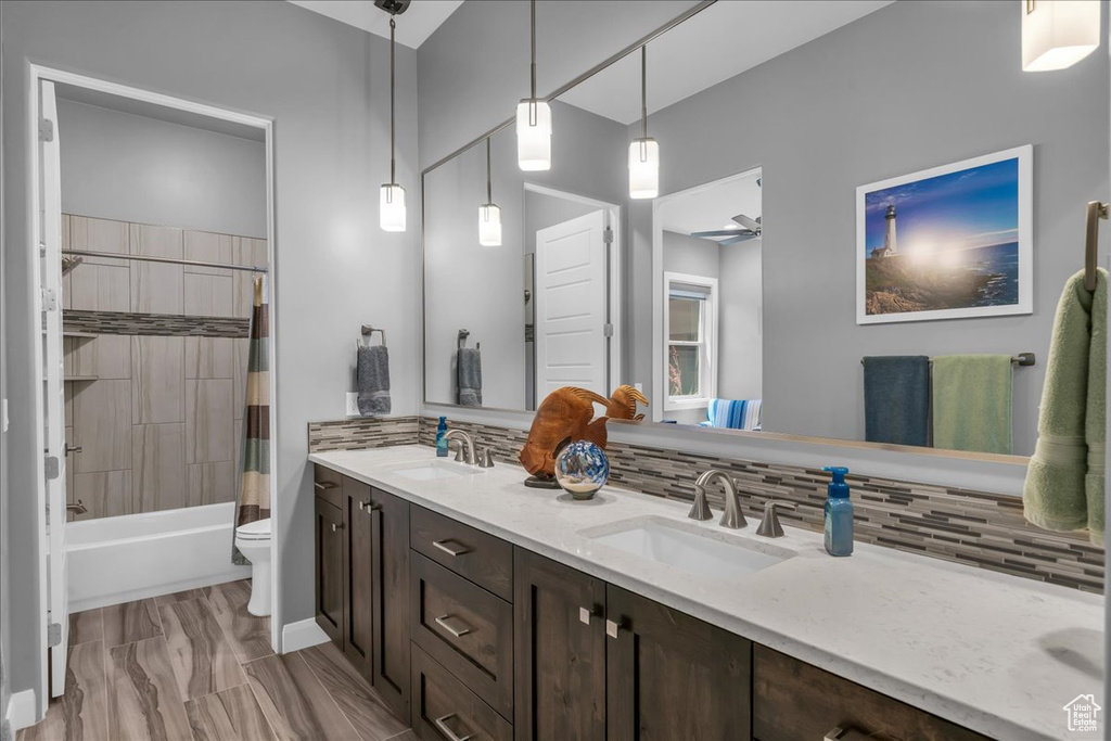 Bathroom with tasteful backsplash, double vanity, toilet, and shower / bathtub combination with curtain