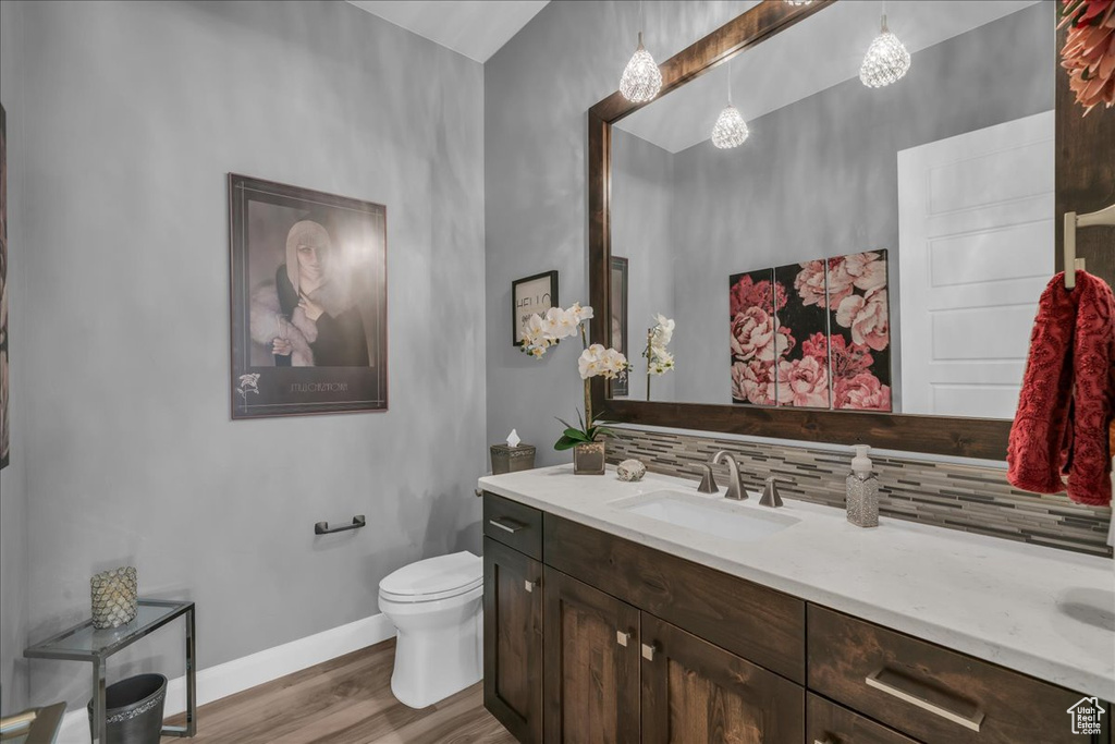 Bathroom featuring decorative backsplash, wood finished floors, vanity, baseboards, and toilet