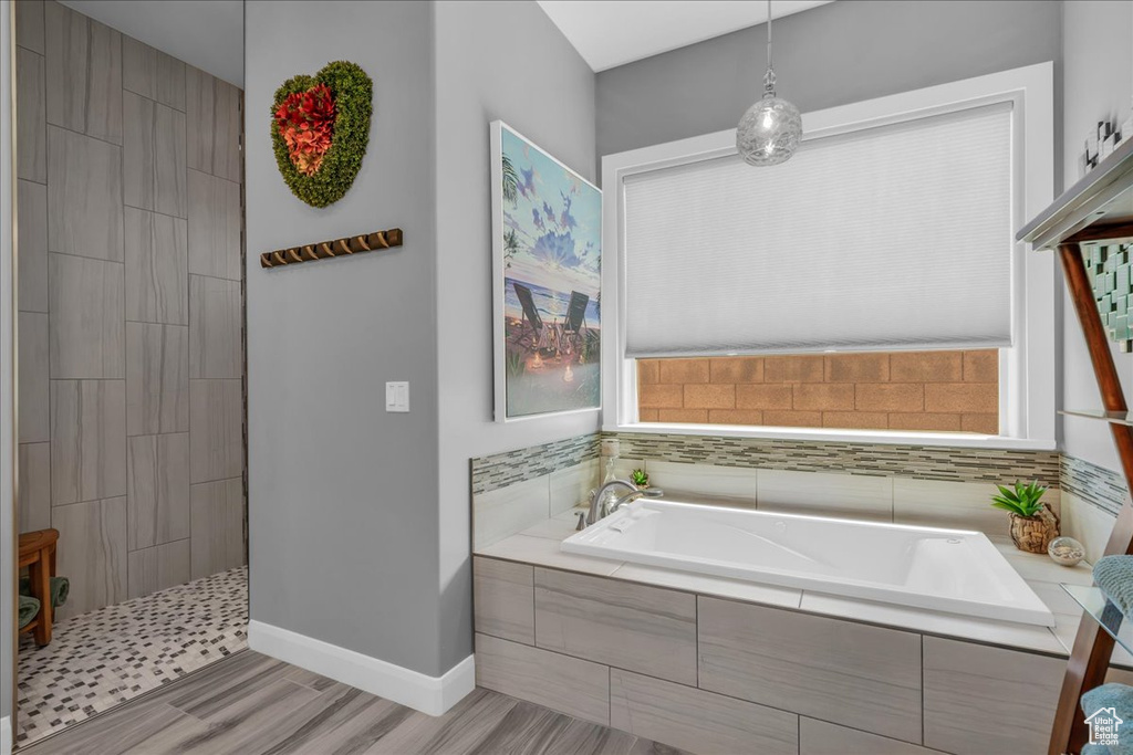 Bathroom featuring a garden tub, wood finished floors, a walk in shower, and baseboards