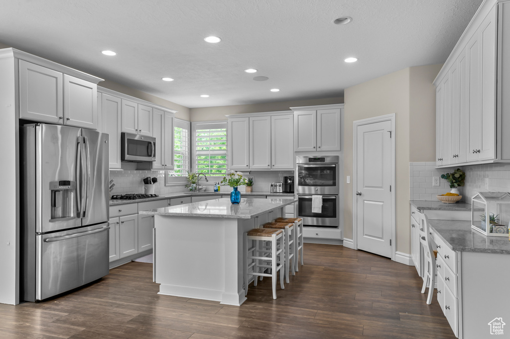 Kitchen featuring stainless steel appliances, a center island, dark wood-style flooring, decorative backsplash, and recessed lighting