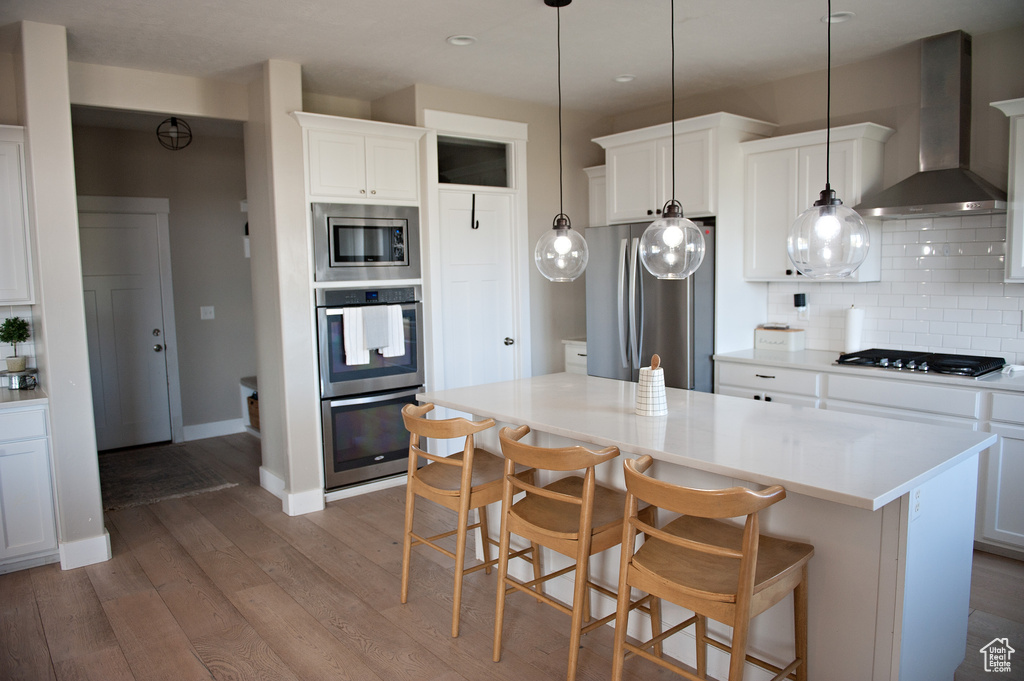 Kitchen featuring wall chimney exhaust hood, stainless steel appliances, recessed lighting, wood finished floors, and backsplash