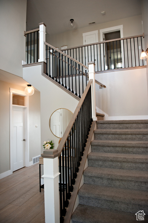 Staircase with wood finished floors, baseboards, and a high ceiling