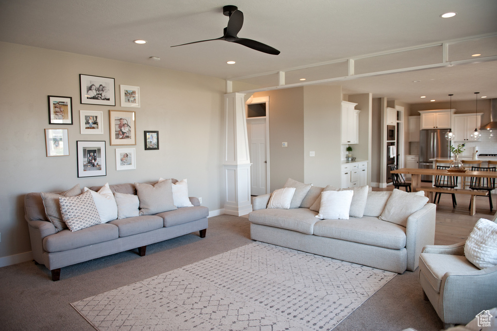 Carpeted living area featuring ornate columns, ceiling fan, recessed lighting, and baseboards