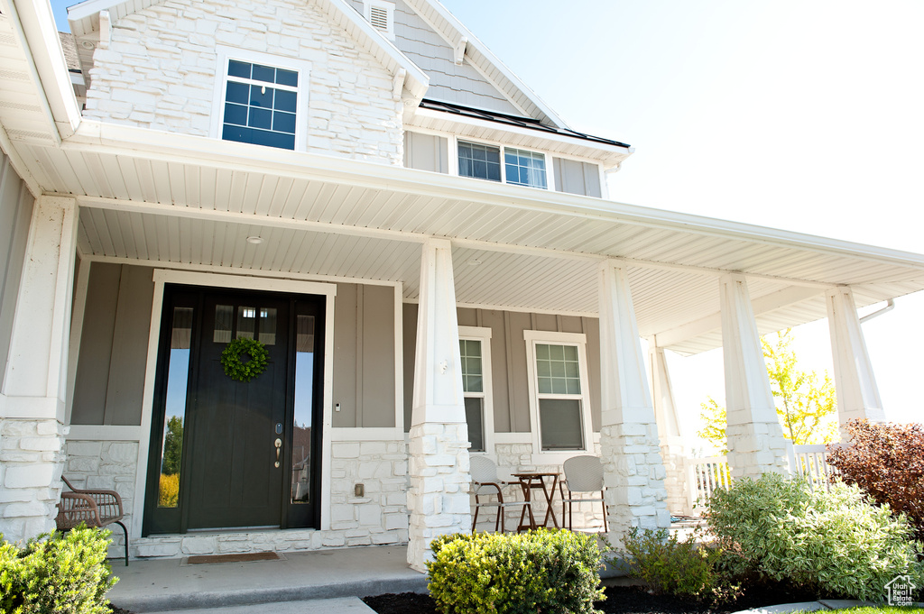 Doorway to property featuring stone siding, a porch, and board and batten siding