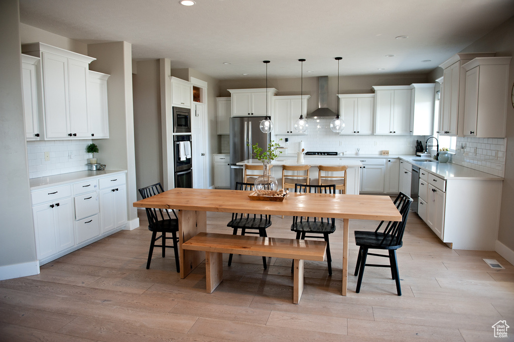 Kitchen featuring wall chimney exhaust hood, a sink, appliances with stainless steel finishes, backsplash, and light wood-type flooring