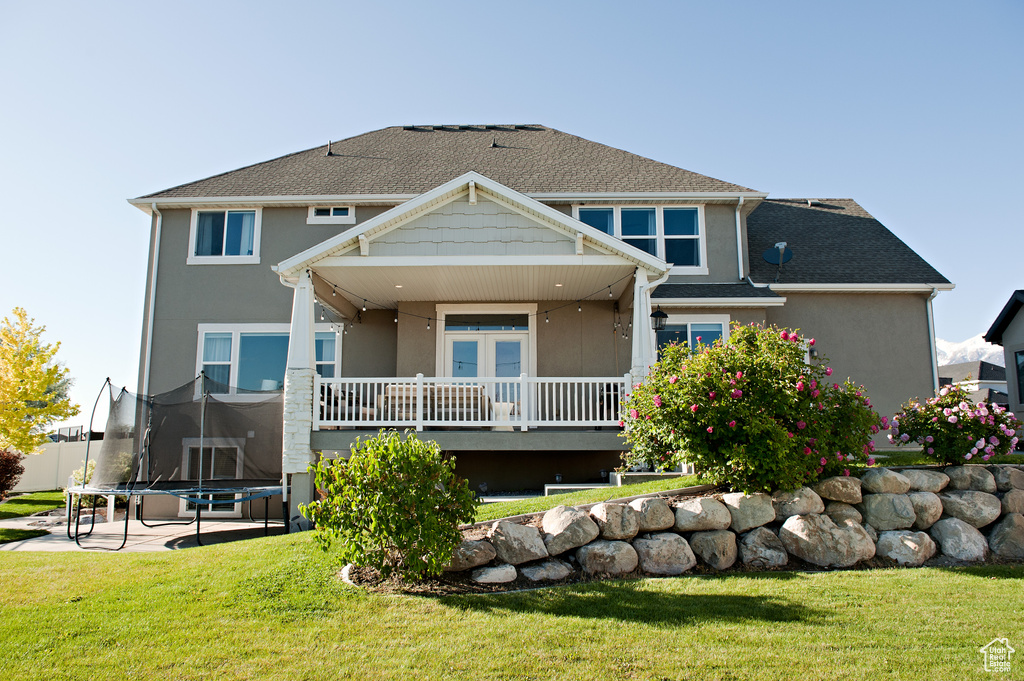 Back of house with a trampoline, stucco siding, and a lawn