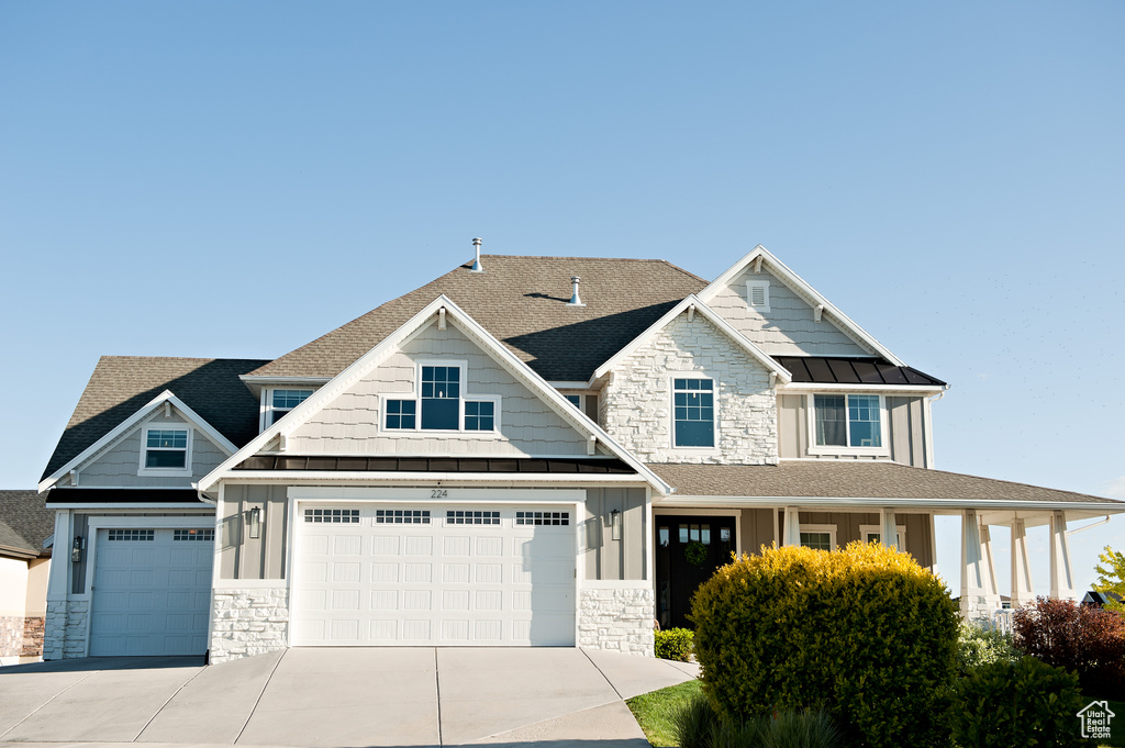Craftsman-style house featuring stone siding, board and batten siding, a standing seam roof, and driveway