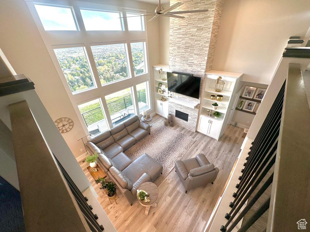 Living area featuring a high ceiling, a stone fireplace, light wood-type flooring, plenty of natural light, and a ceiling fan