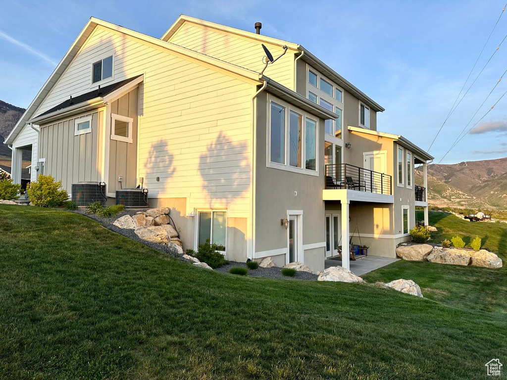 Rear view of property with a balcony, a lawn, and central AC unit