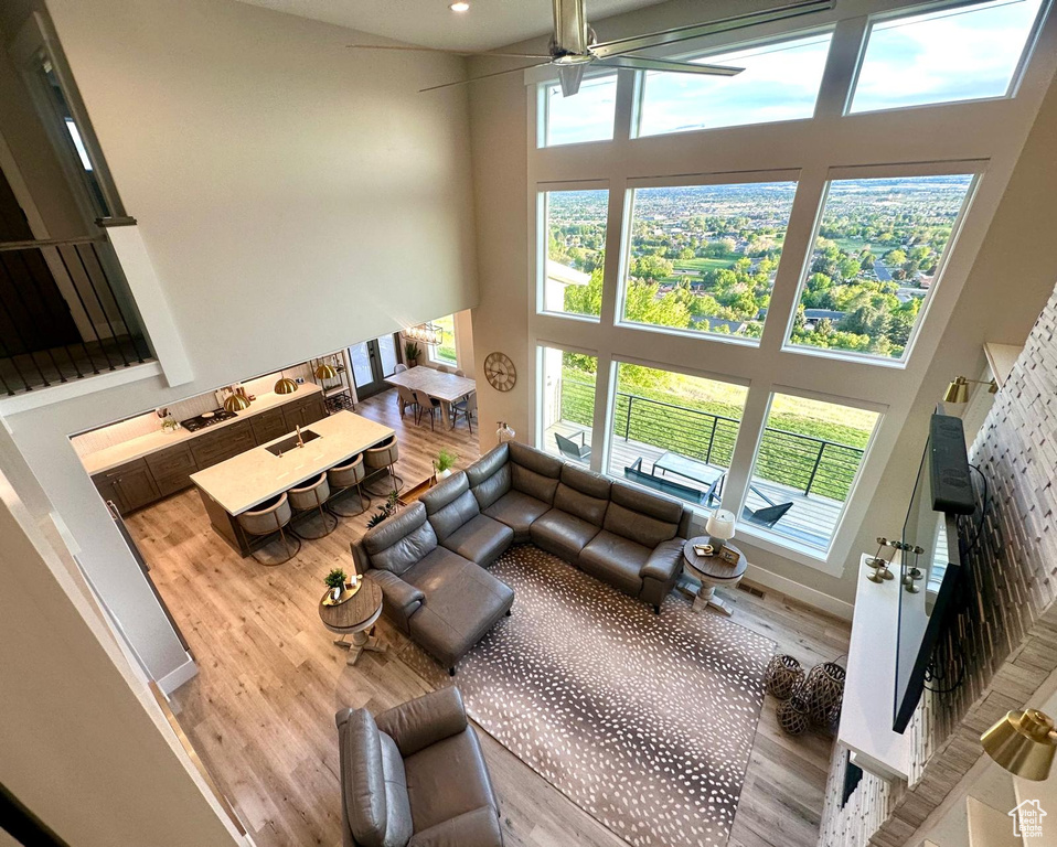 Living area with a high ceiling, wood finished floors, a ceiling fan, healthy amount of natural light, and recessed lighting