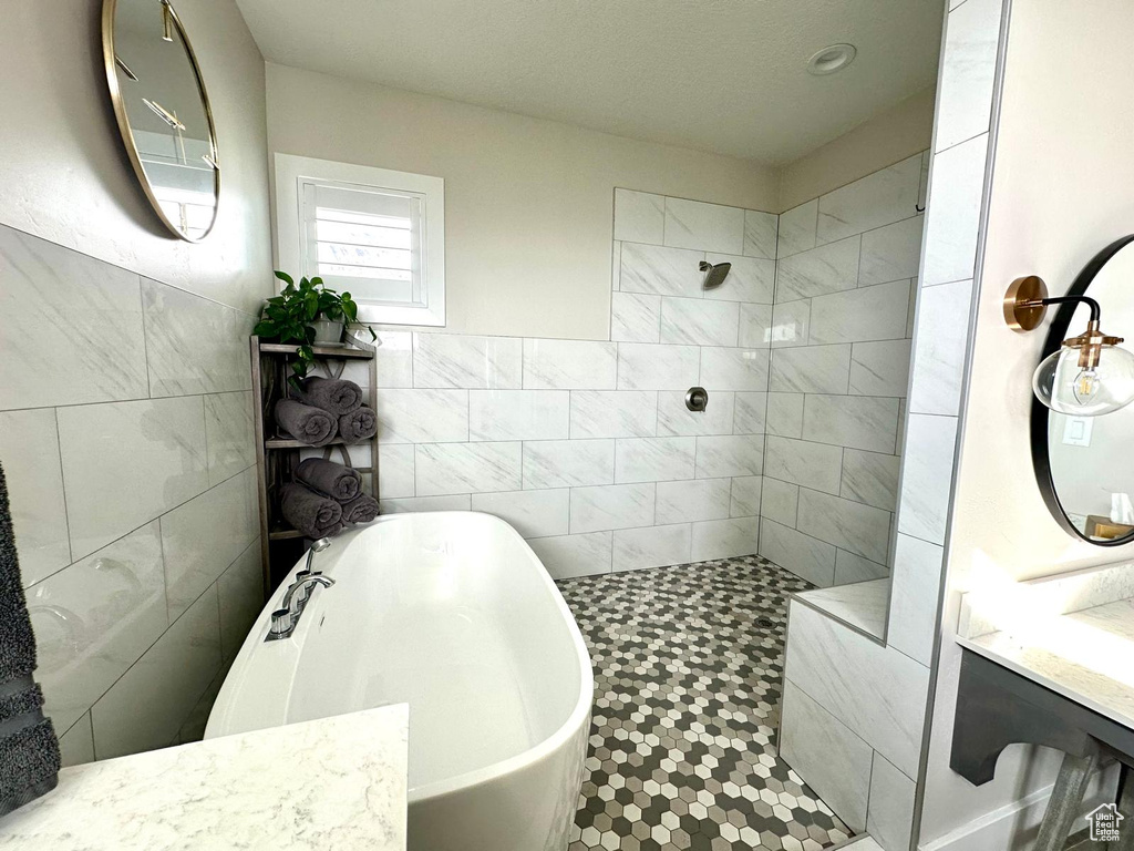 Full bath featuring tile walls, a soaking tub, tiled shower, and vanity