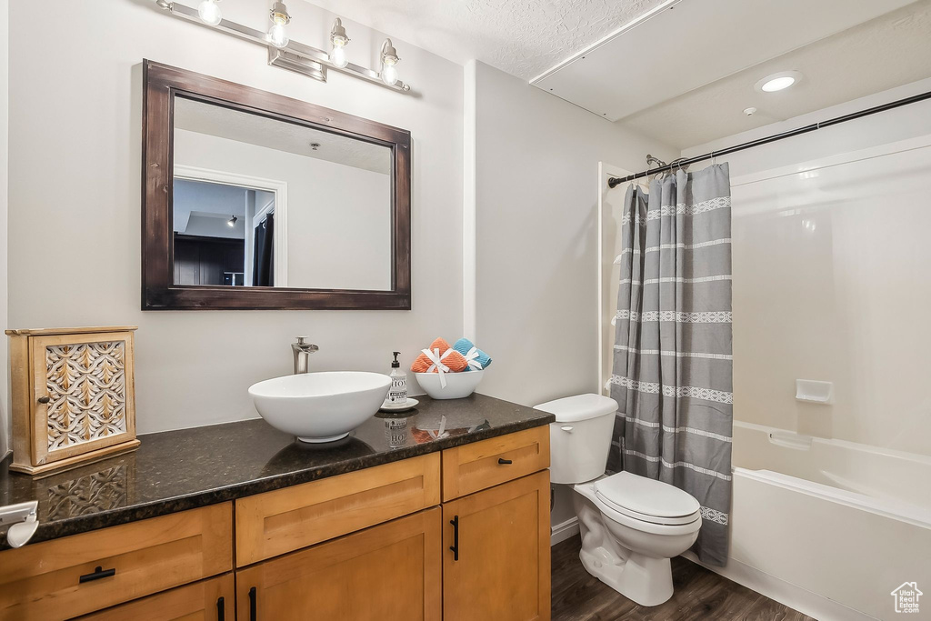 Full bathroom with wood finished floors, toilet, vanity, and shower / tub combo with curtain