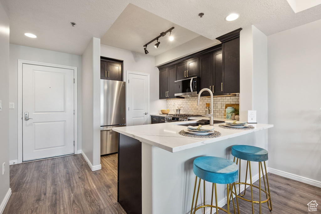 Kitchen with stainless steel appliances, baseboards, dark wood finished floors, decorative backsplash, and a peninsula