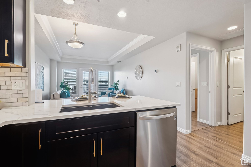 Kitchen with stainless steel dishwasher, dark cabinetry, a raised ceiling, open floor plan, and a sink
