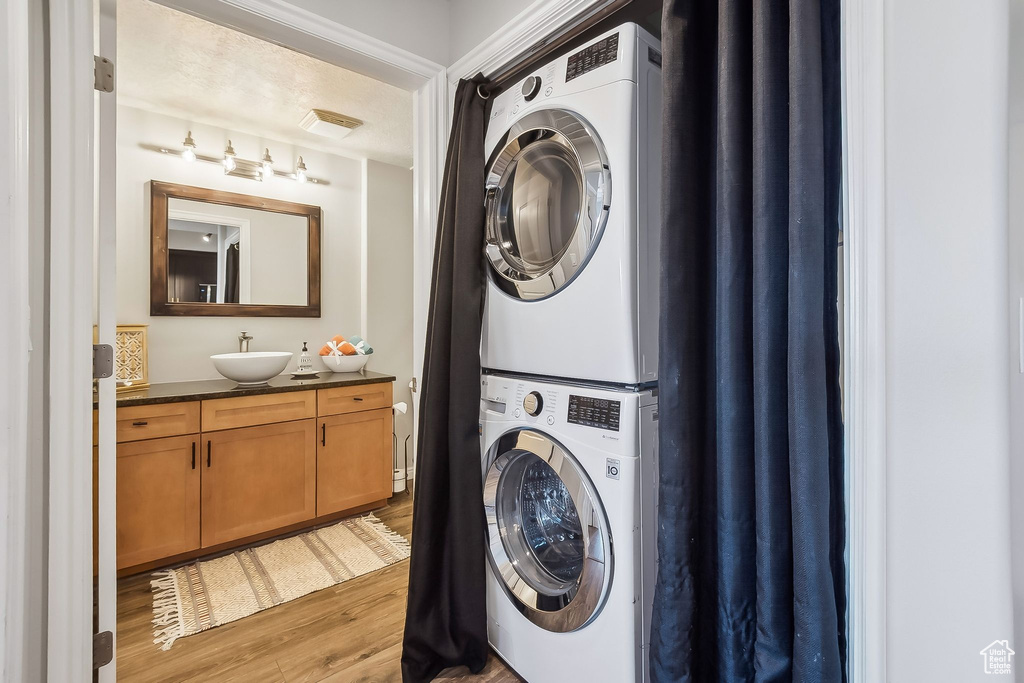 Clothes washing area featuring stacked washer / drying machine, light wood finished floors, and a sink