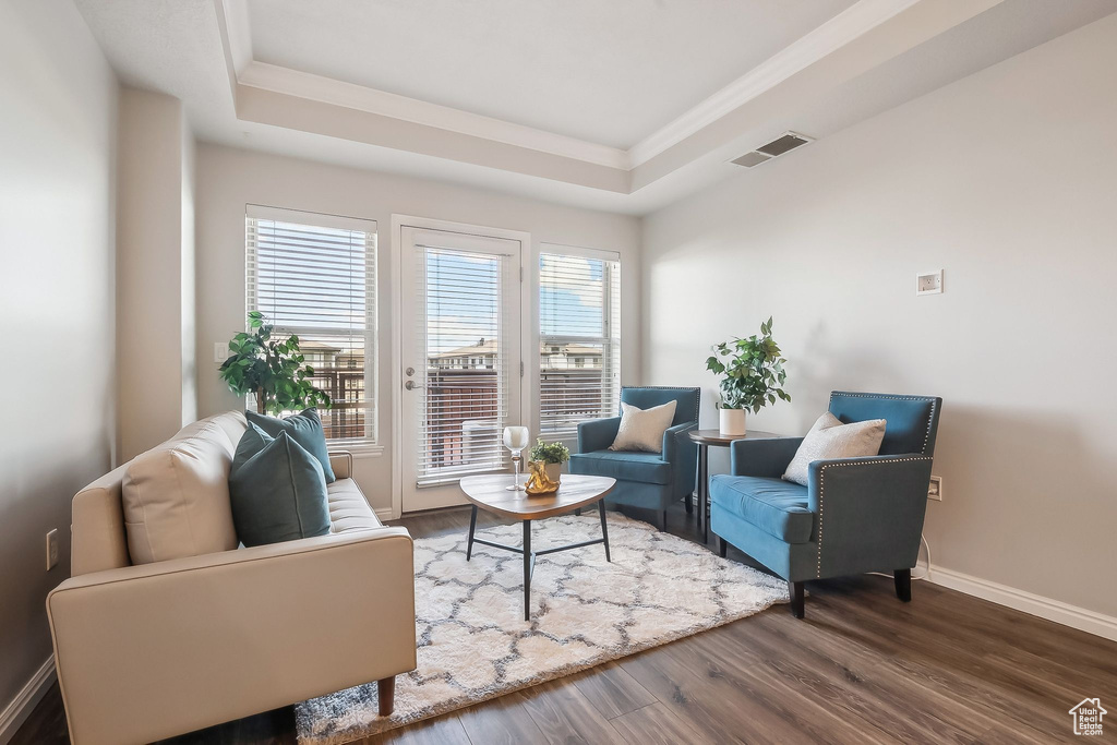 Living area with a tray ceiling, baseboards, dark wood-type flooring, and ornamental molding