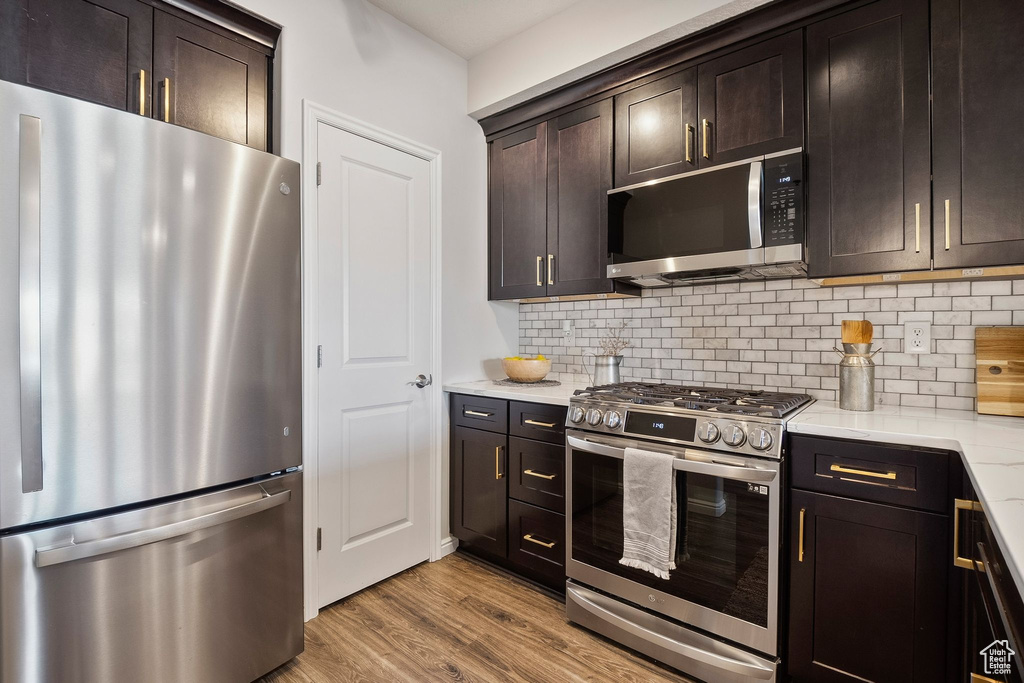 Kitchen with stainless steel appliances, decorative backsplash, light wood-style floors, and dark brown cabinetry