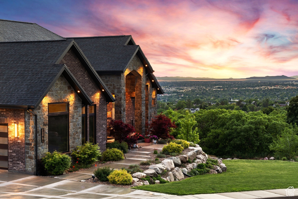 View of front of property featuring stone siding, roof with shingles, a yard, brick siding, and a mountain view