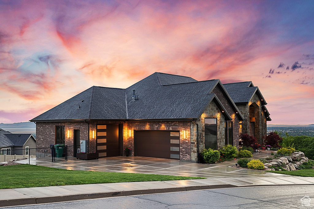 View of front facade featuring an attached garage, brick siding, driveway, and stone siding