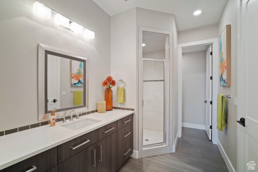 Full bathroom with a stall shower, vanity, baseboards, wood finished floors, and recessed lighting