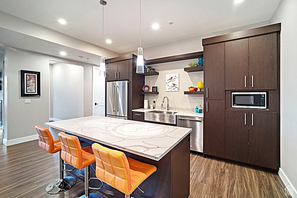 Kitchen featuring stainless steel appliances, a sink, open shelves, dark brown cabinets, and baseboards
