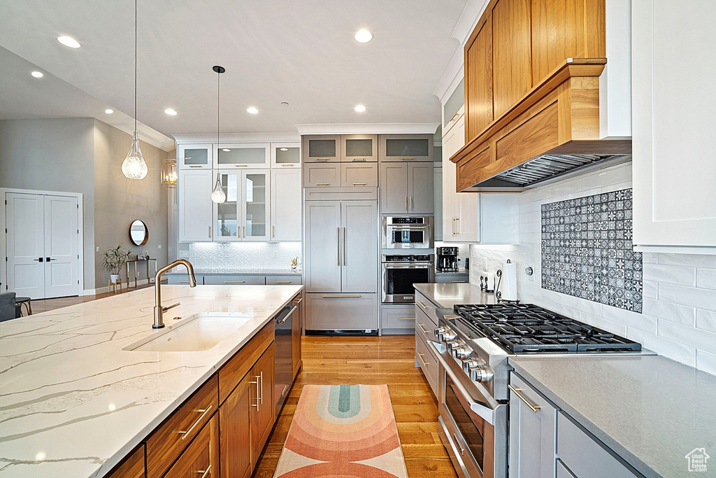 Kitchen featuring high quality appliances, a sink, premium range hood, recessed lighting, and light stone counters