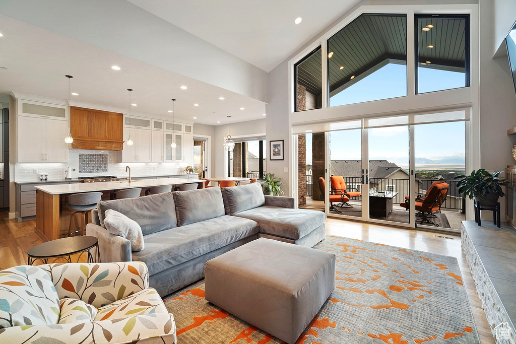 Living area featuring light wood-style flooring, a towering ceiling, and recessed lighting
