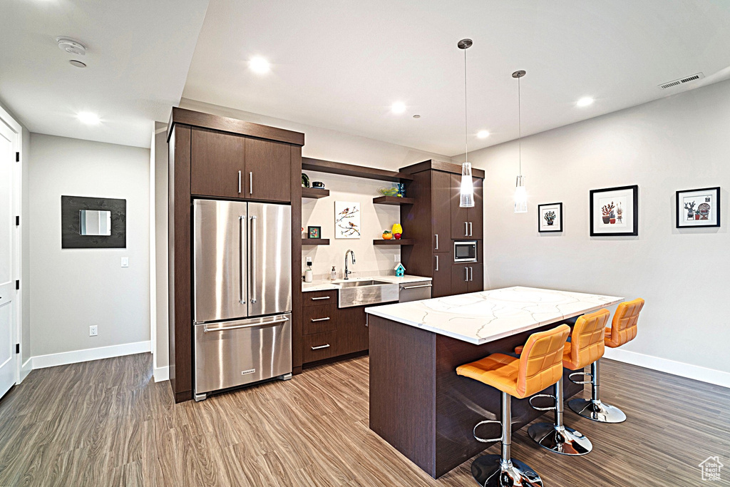 Kitchen featuring stainless steel appliances, a sink, wood finished floors, dark brown cabinetry, and recessed lighting