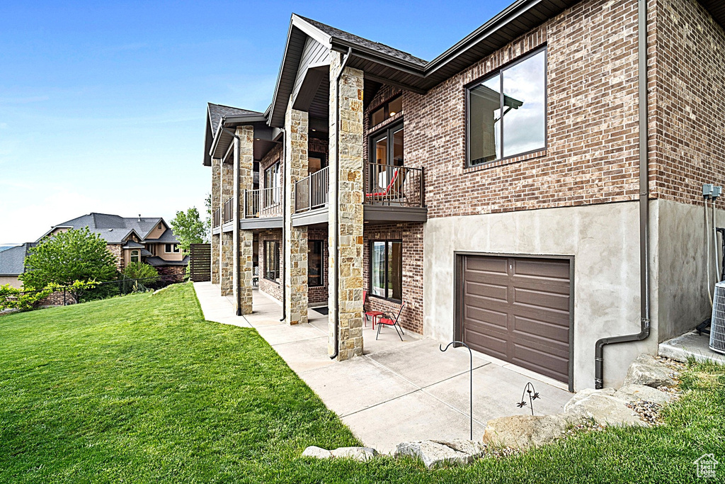 View of front of house with a balcony, a front yard, stone siding, a garage, and brick siding