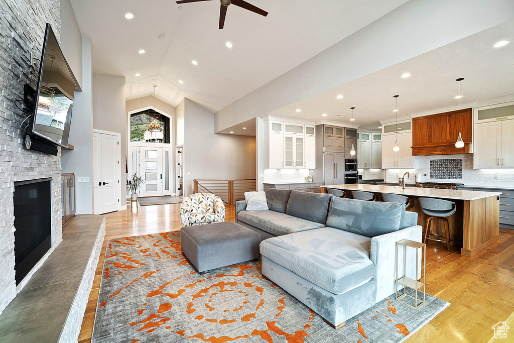 Living area with light wood-style flooring, a ceiling fan, recessed lighting, a stone fireplace, and high vaulted ceiling