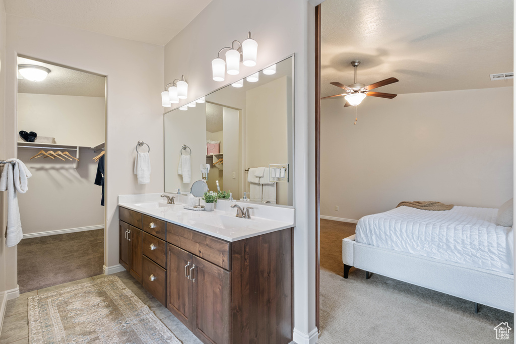 Bathroom featuring ceiling fan, double vanity, a spacious closet, and baseboards