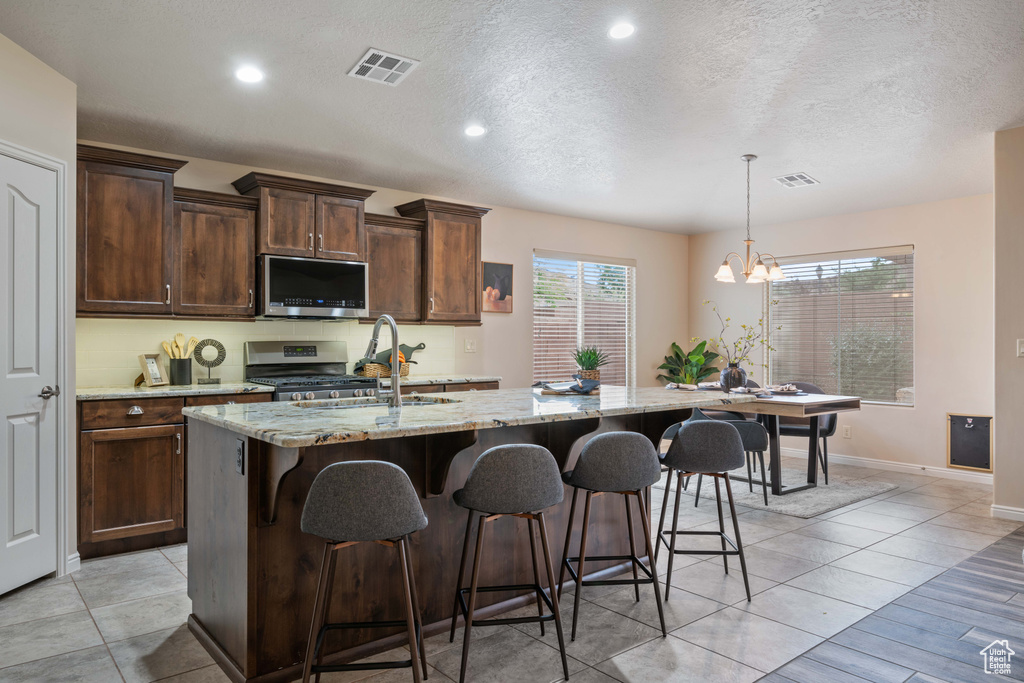 Kitchen featuring stainless steel appliances, a center island with sink, light stone counters, a breakfast bar, and a chandelier
