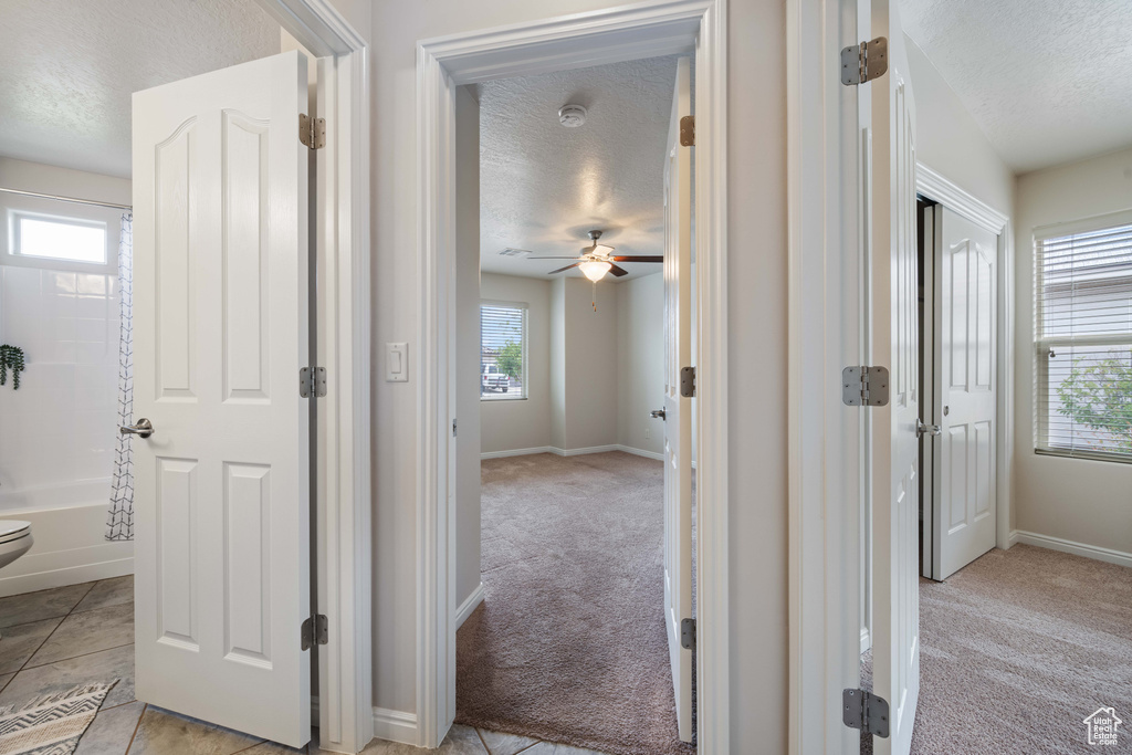 Hallway featuring a textured ceiling, light carpet, and baseboards