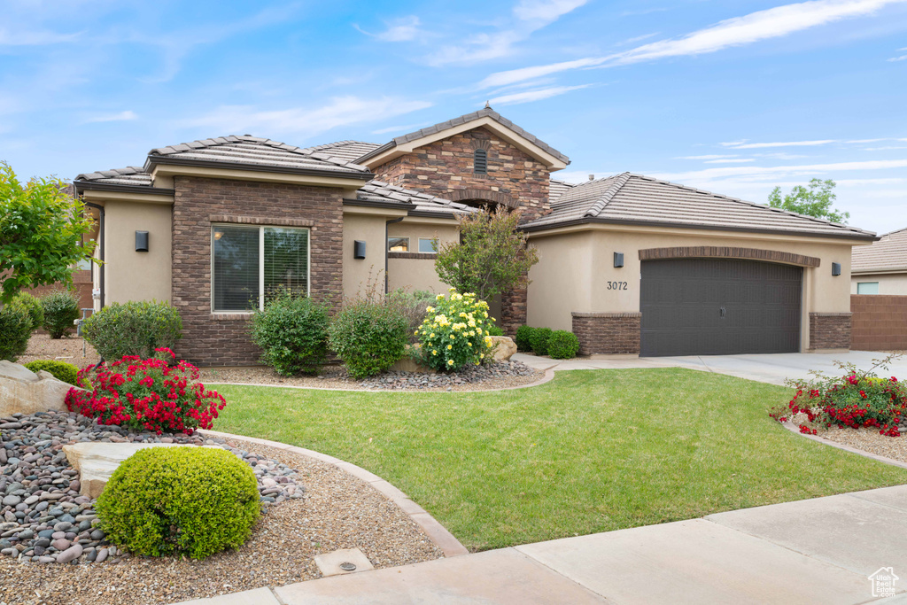 View of front of home with an attached garage, stucco siding, a tile roof, and a front yard