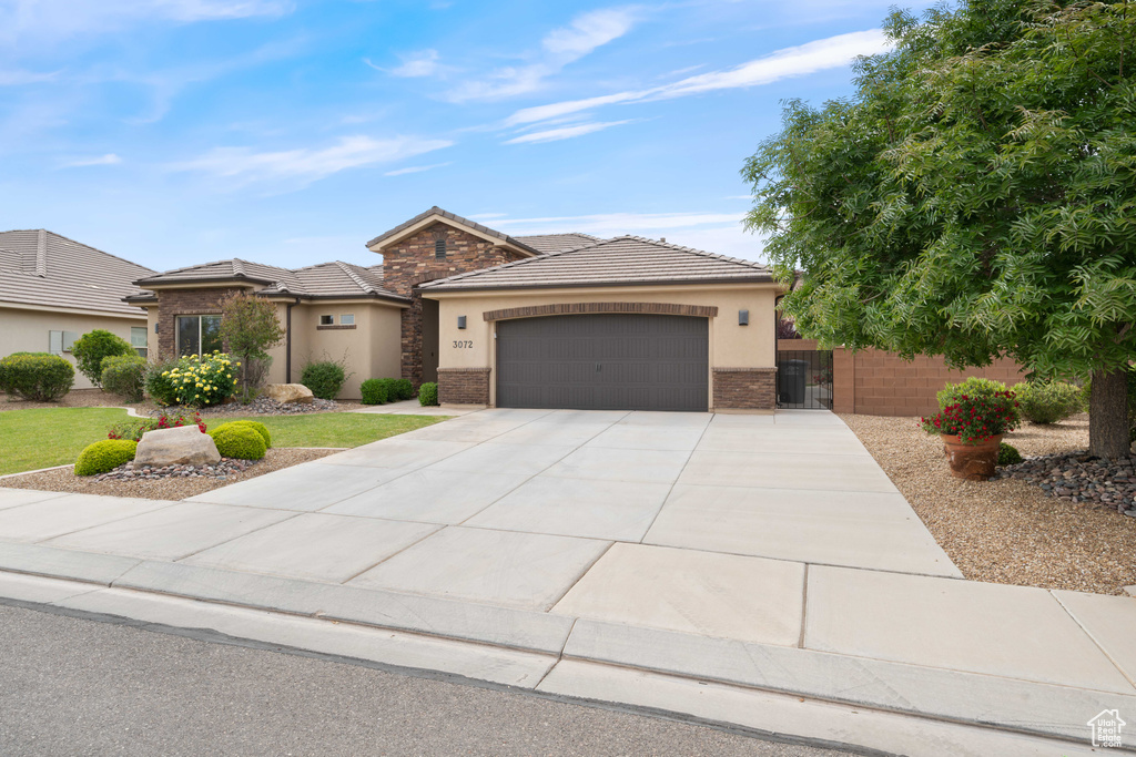 View of front of property featuring an attached garage, stucco siding, concrete driveway, and a tile roof