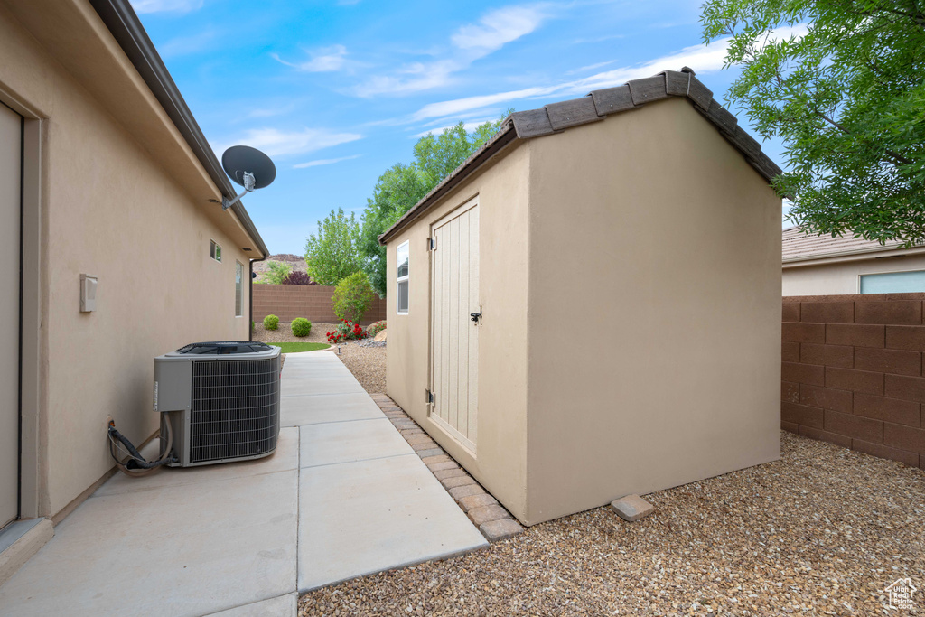 View of side of property featuring central AC unit, a fenced backyard, stucco siding, and an outbuilding