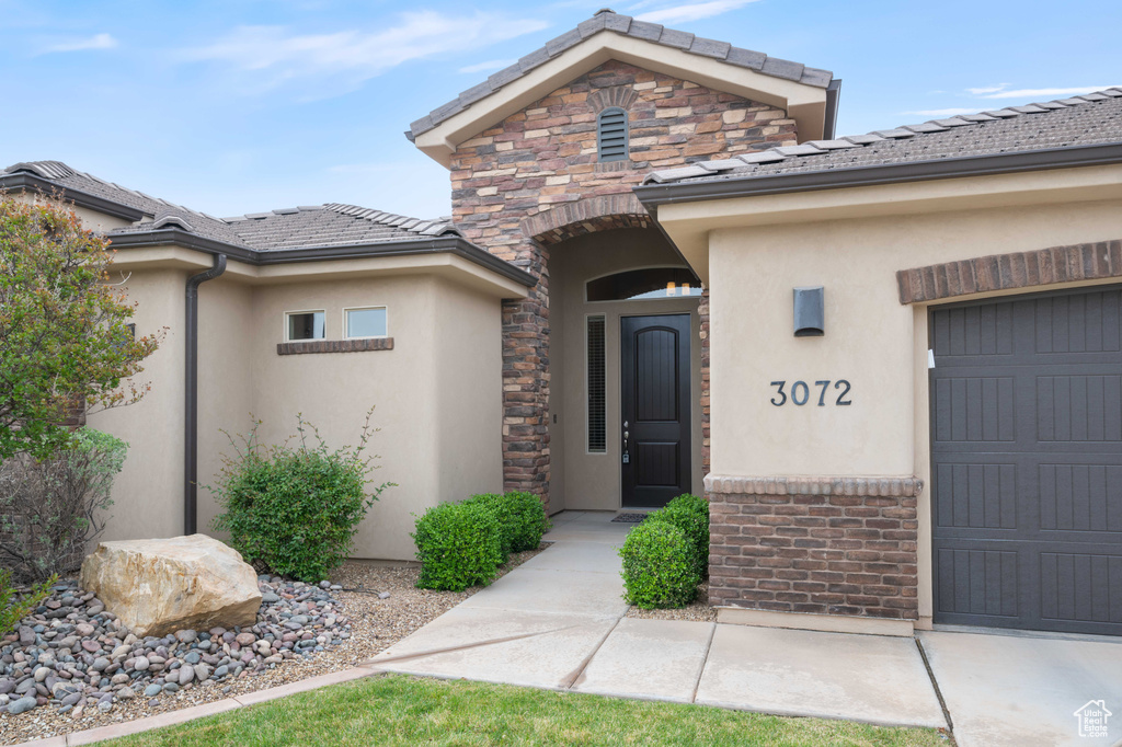 View of exterior entry featuring an attached garage, stucco siding, and stone siding