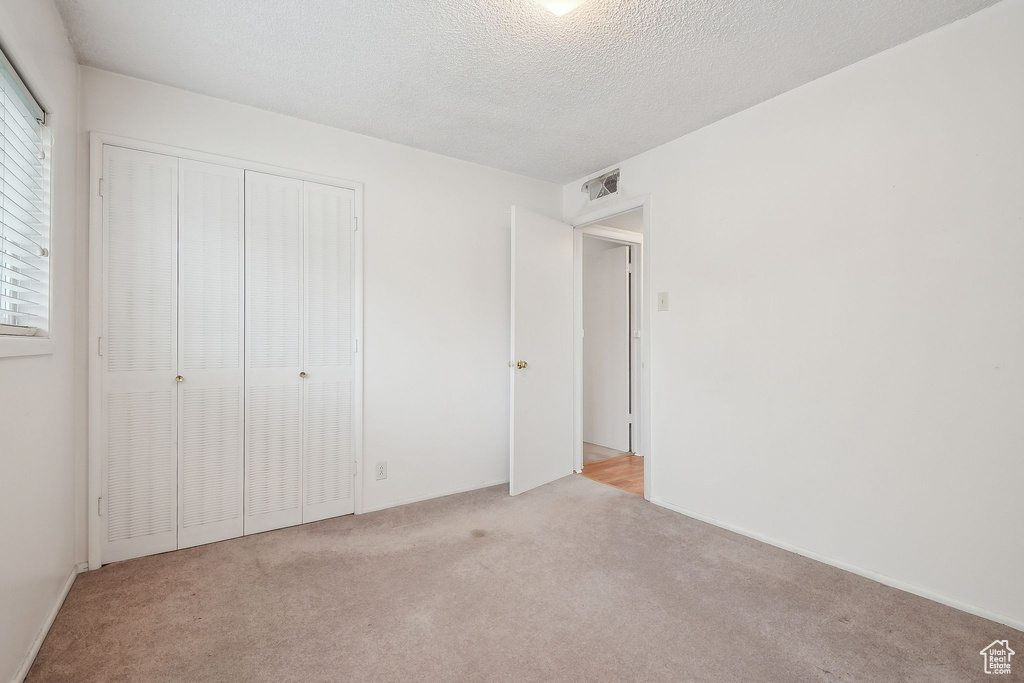 Unfurnished bedroom with carpet floors, a closet, multiple windows, and a textured ceiling