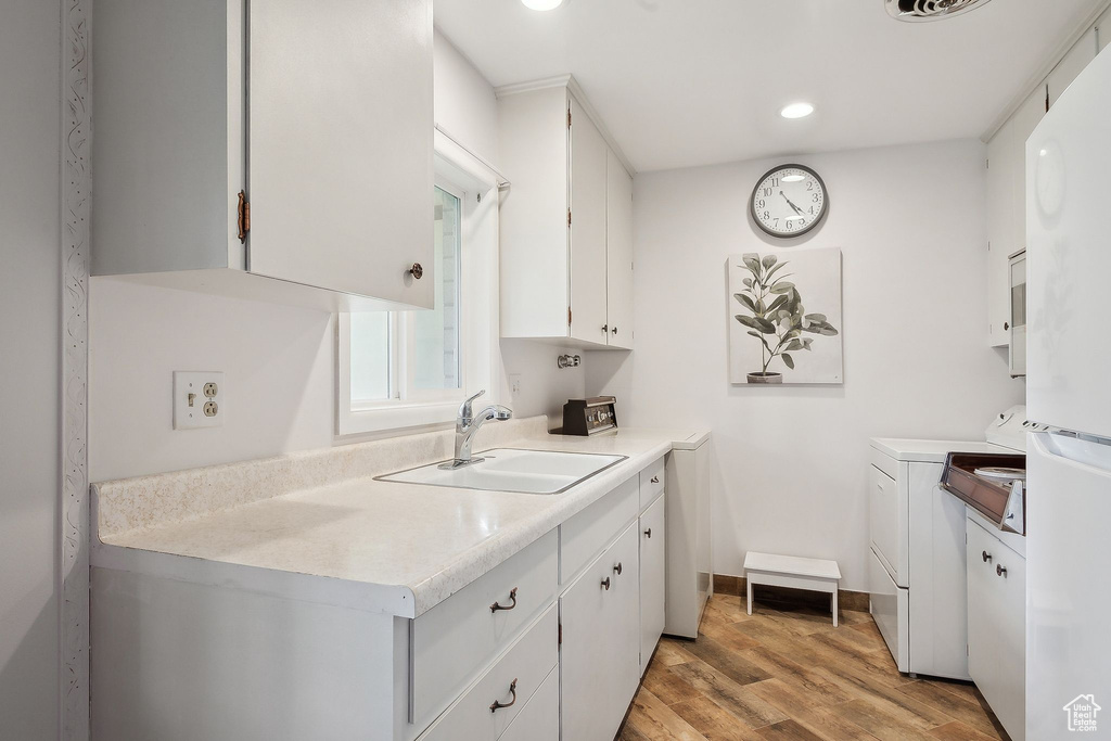 Kitchen featuring a sink, separate washer and dryer, white cabinets, light wood-type flooring, and freestanding refrigerator