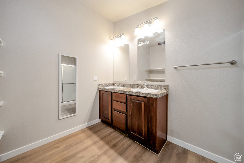 Full bath with wood finished floors, double vanity, and a shower