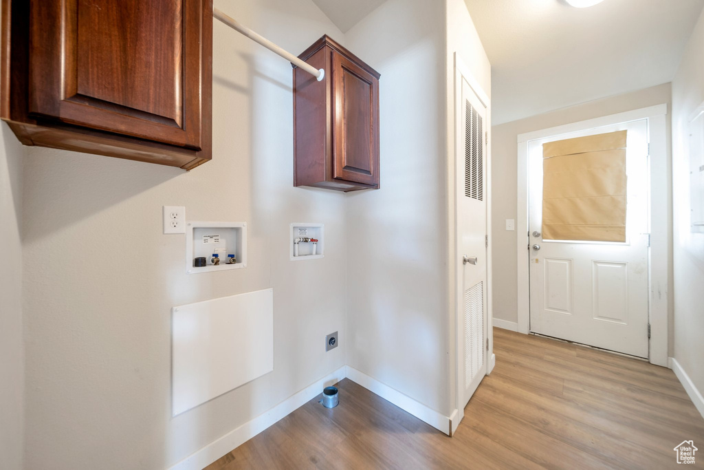 Washroom with electric dryer hookup, hookup for a washing machine, light wood-style floors, and cabinet space