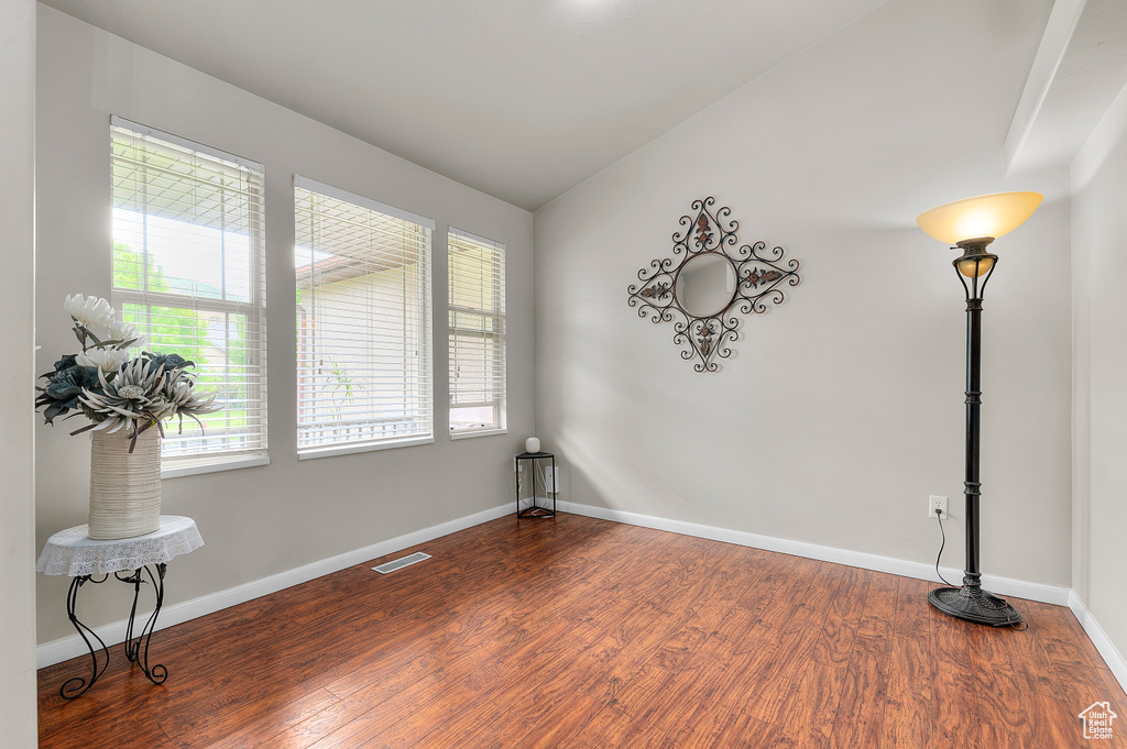 Spare room featuring dark wood-type flooring, baseboards, and lofted ceiling