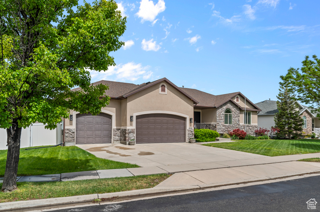 View of front of property featuring a garage, stucco siding, stone siding, a front yard, and concrete driveway