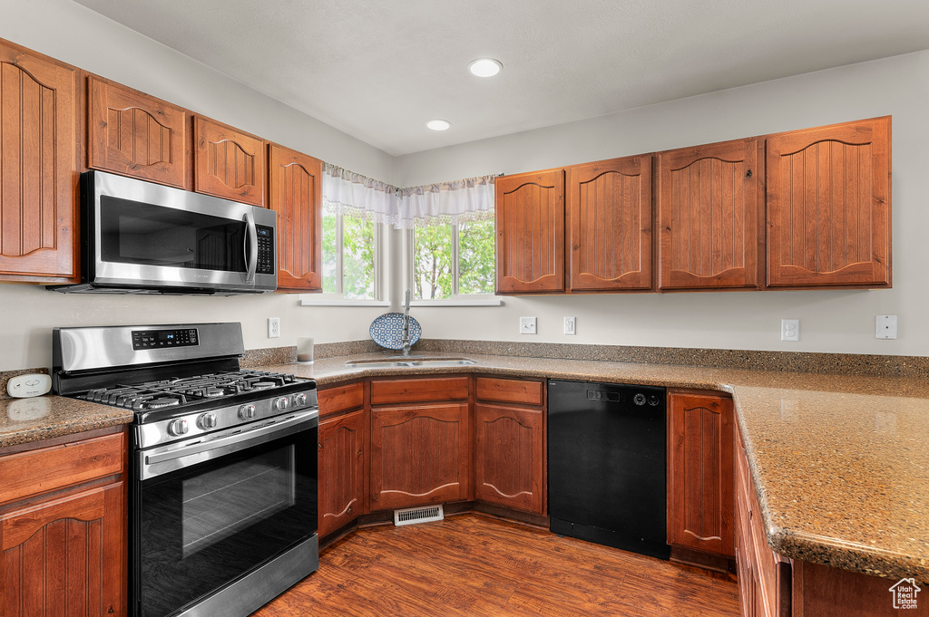 Kitchen with stainless steel appliances, recessed lighting, dark wood-type flooring, brown cabinets, and a sink
