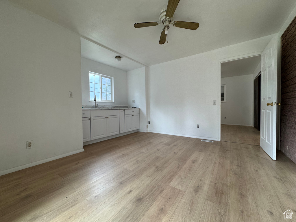 Unfurnished living room with a sink, ceiling fan, light wood finished floors, and baseboards