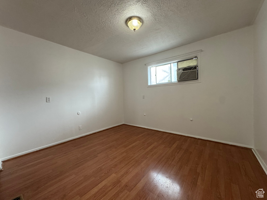 Empty room featuring wood finished floors, baseboards, a textured ceiling, and cooling unit