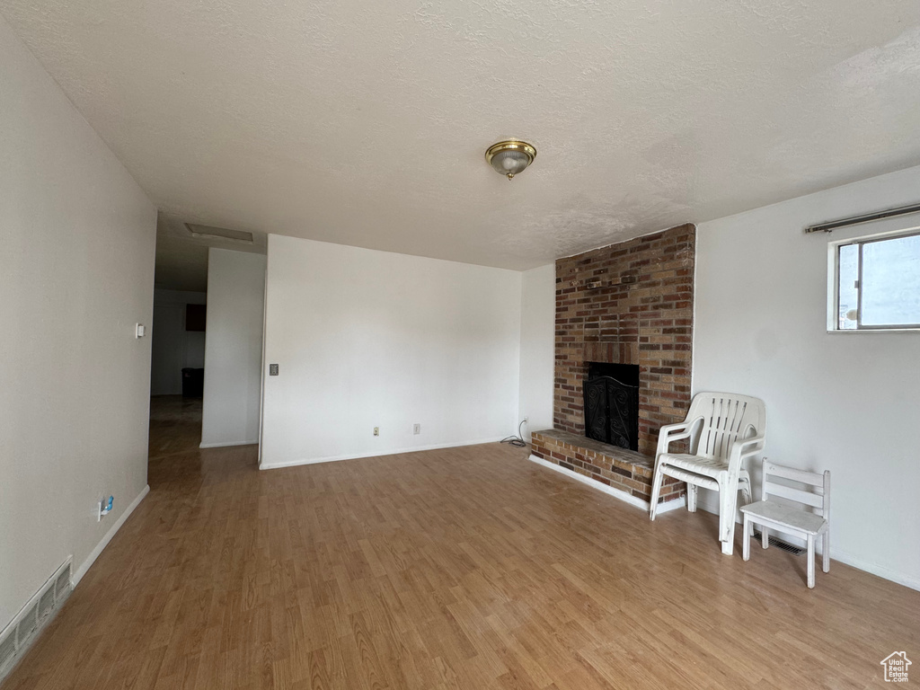 Unfurnished living room featuring light wood-type flooring, a textured ceiling, a brick fireplace, and baseboards